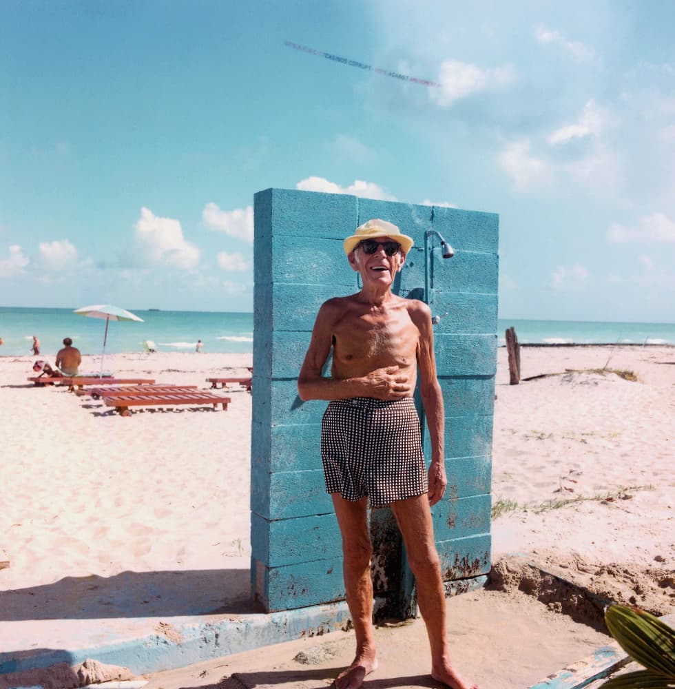 A beachgoer smiles from an outdoor shower. 